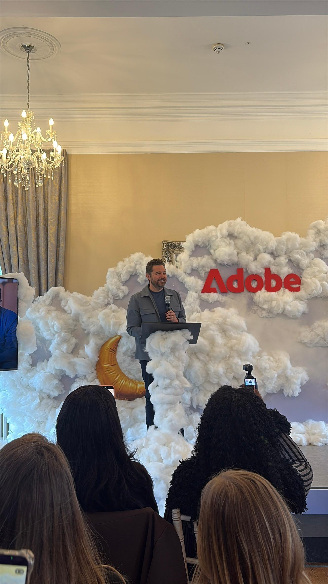 Daniel Priestley speaking at a lectern in front of a cloud installation and an Adobe sign